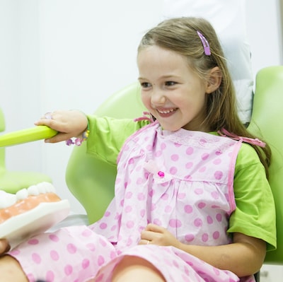 Little girl wearing a pink dental bib and holding a giant toothbrush