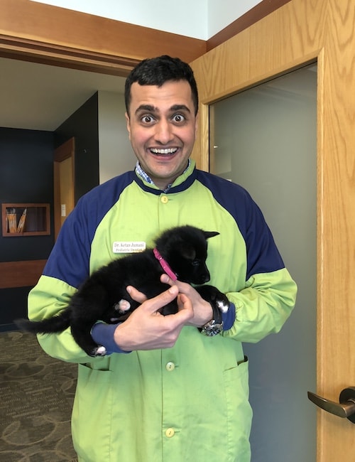 Dr. Ketan Jumani holding a giant toothbrush and smiling while wearing a coat