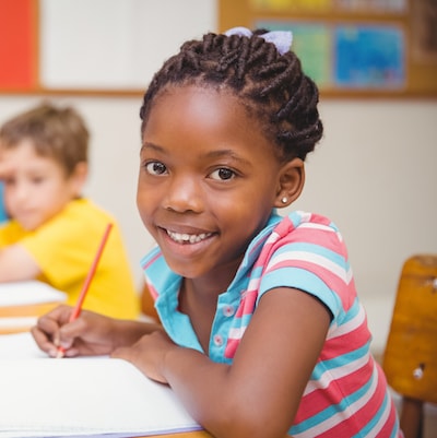 Young girl drawing with a red pencil at a desk