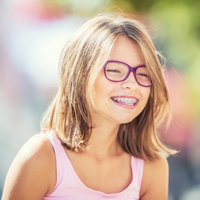 Girl wearing pink glasses and smiling to show her braces