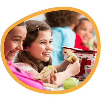 A smiling girl eating her school lunch with children on the background